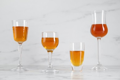 Photo of Different delicious liqueurs in glasses on white marble table