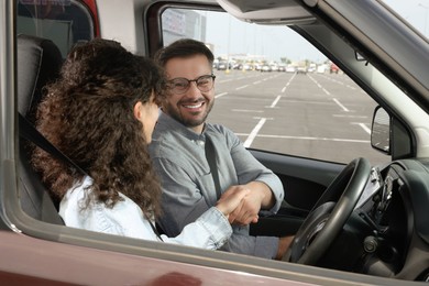 Photo of Driving school. Happy student shaking hands with driving instructor during lesson in car at parking lot