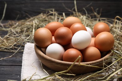 Photo of Fresh chicken eggs in bowl and dried hay on black wooden table