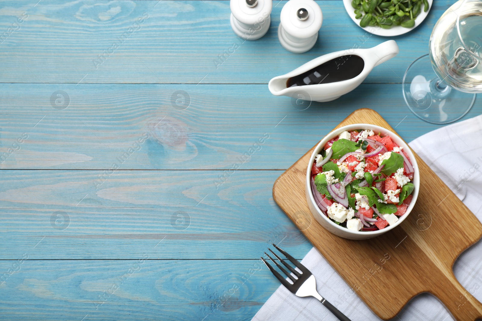 Photo of Delicious salad with watermelon, red onion, arugula and feta cheese served on light blue wooden table, flat lay. Space for text