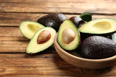 Photo of Whole and cut avocados on wooden table, closeup