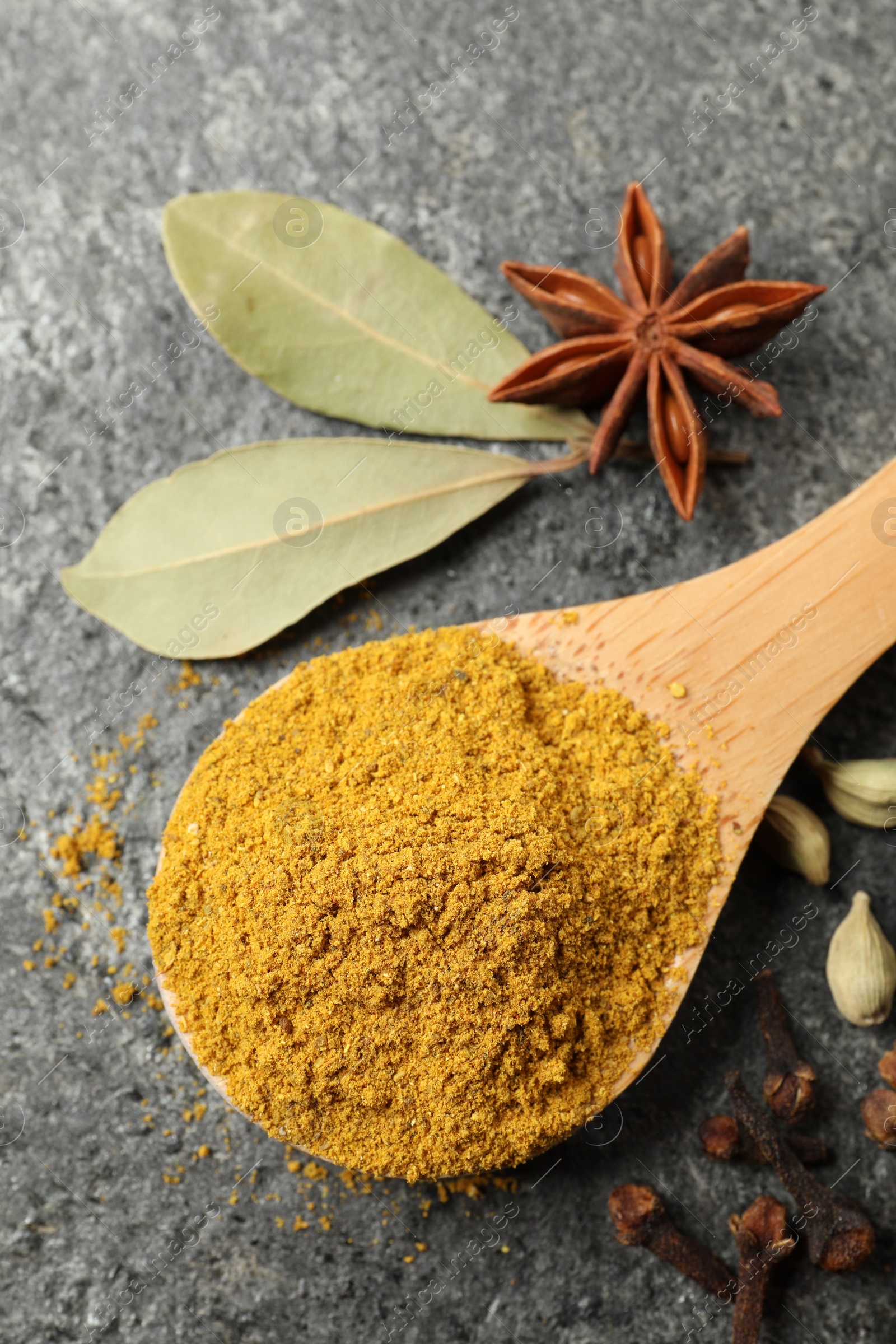 Photo of Spoon with dry curry powder and other spices on dark textured table, flat lay