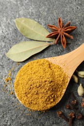 Photo of Spoon with dry curry powder and other spices on dark textured table, flat lay