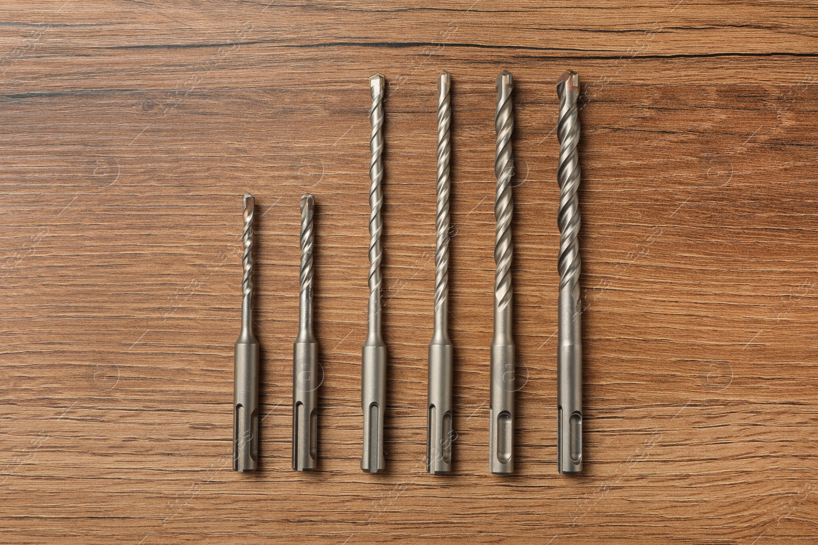 Photo of Different drill bits on wooden table, flat lay