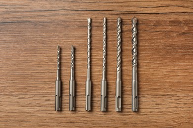 Photo of Different drill bits on wooden table, flat lay