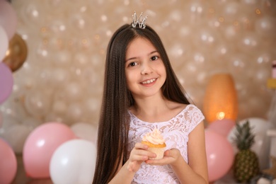 Photo of Happy little girl with birthday cupcake in beautifully decorated room at home