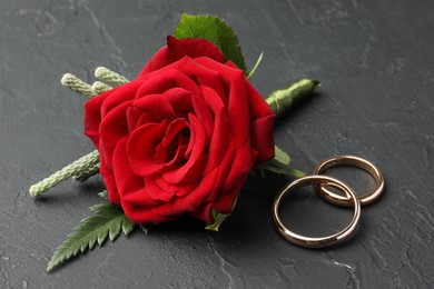 Photo of Stylish red boutonniere and rings on black table, closeup