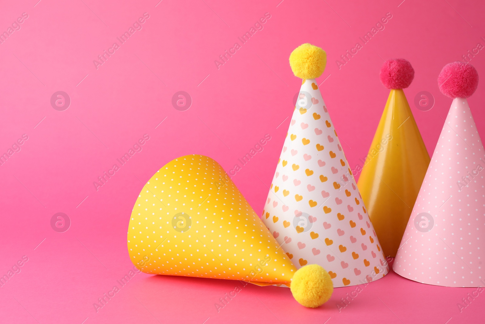 Photo of Beautiful party hats with pompoms on pink background