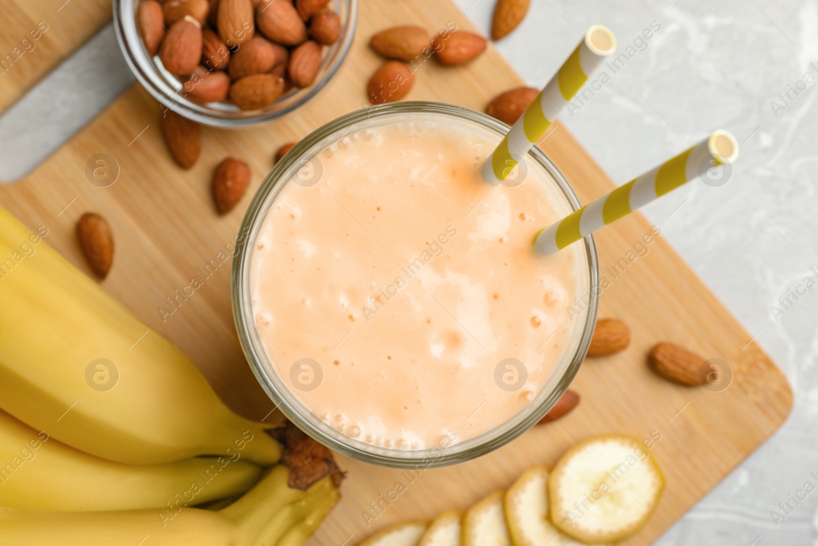 Photo of Flat lay composition of banana smoothie in glass and nuts on light grey table