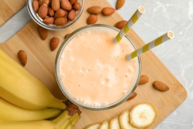 Flat lay composition of banana smoothie in glass and nuts on light grey table