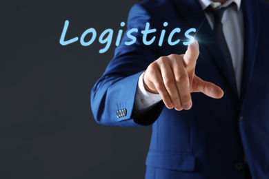 Businessman pointing at word LOGISTICS on virtual screen against dark background, closeup 
