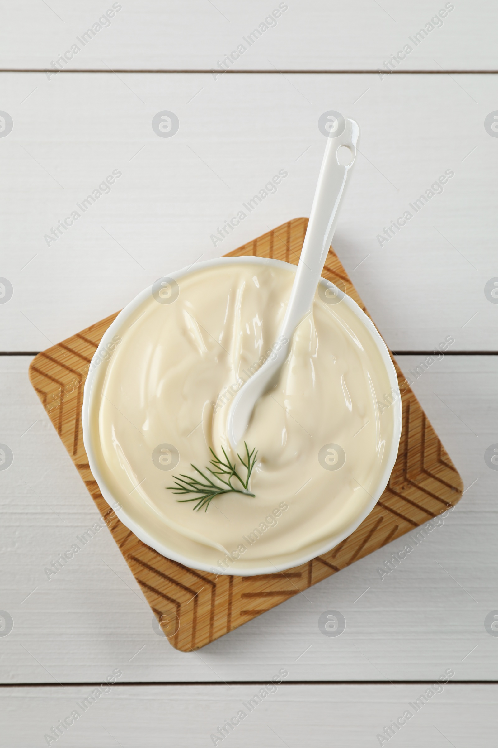 Photo of Fresh mayonnaise sauce in bowl on white wooden table, top view