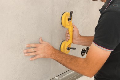 Photo of Worker installing wall tiles with vacuum holder indoors, closeup