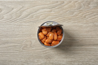 Photo of Open tin can of beans on wooden background, top view