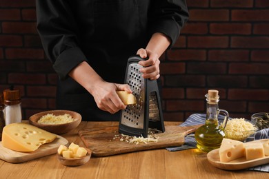 Photo of Woman grating cheese at wooden table, closeup