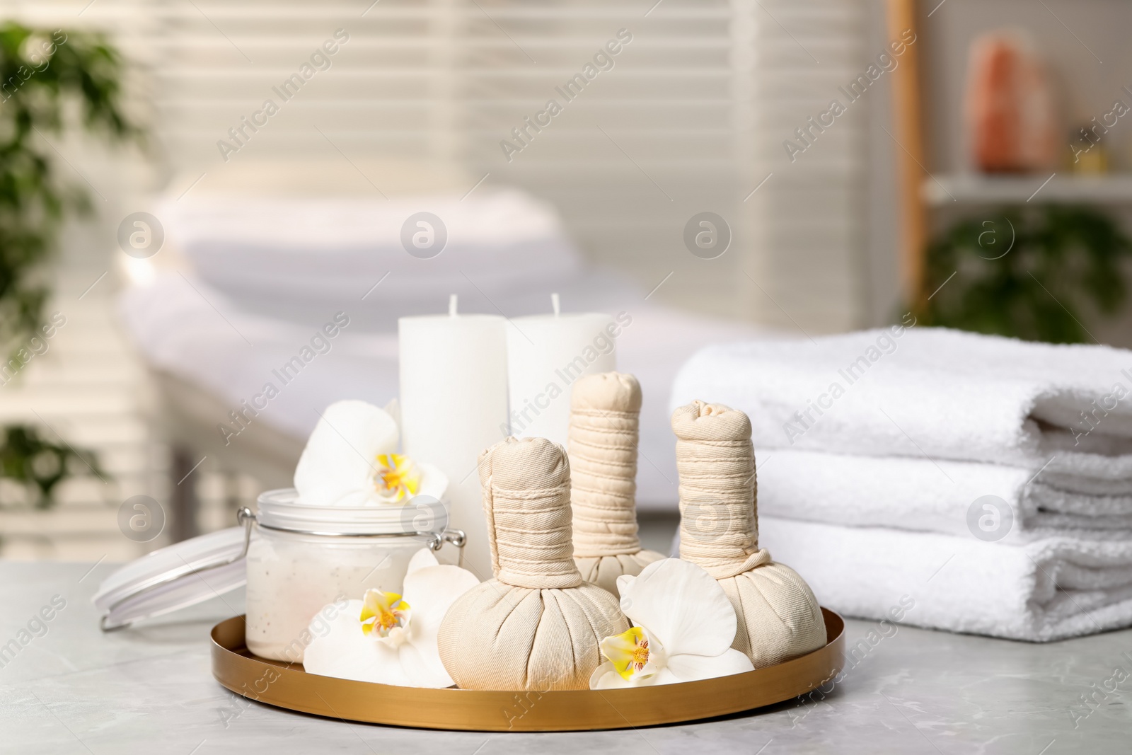 Photo of Tray with herbal bags, candles, scrub, beautiful flowers and folded towels on grey marble table in salon, space for text. Spa products