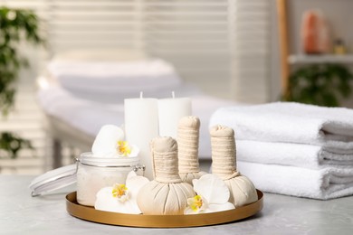 Photo of Tray with herbal bags, candles, scrub, beautiful flowers and folded towels on grey marble table in salon, space for text. Spa products