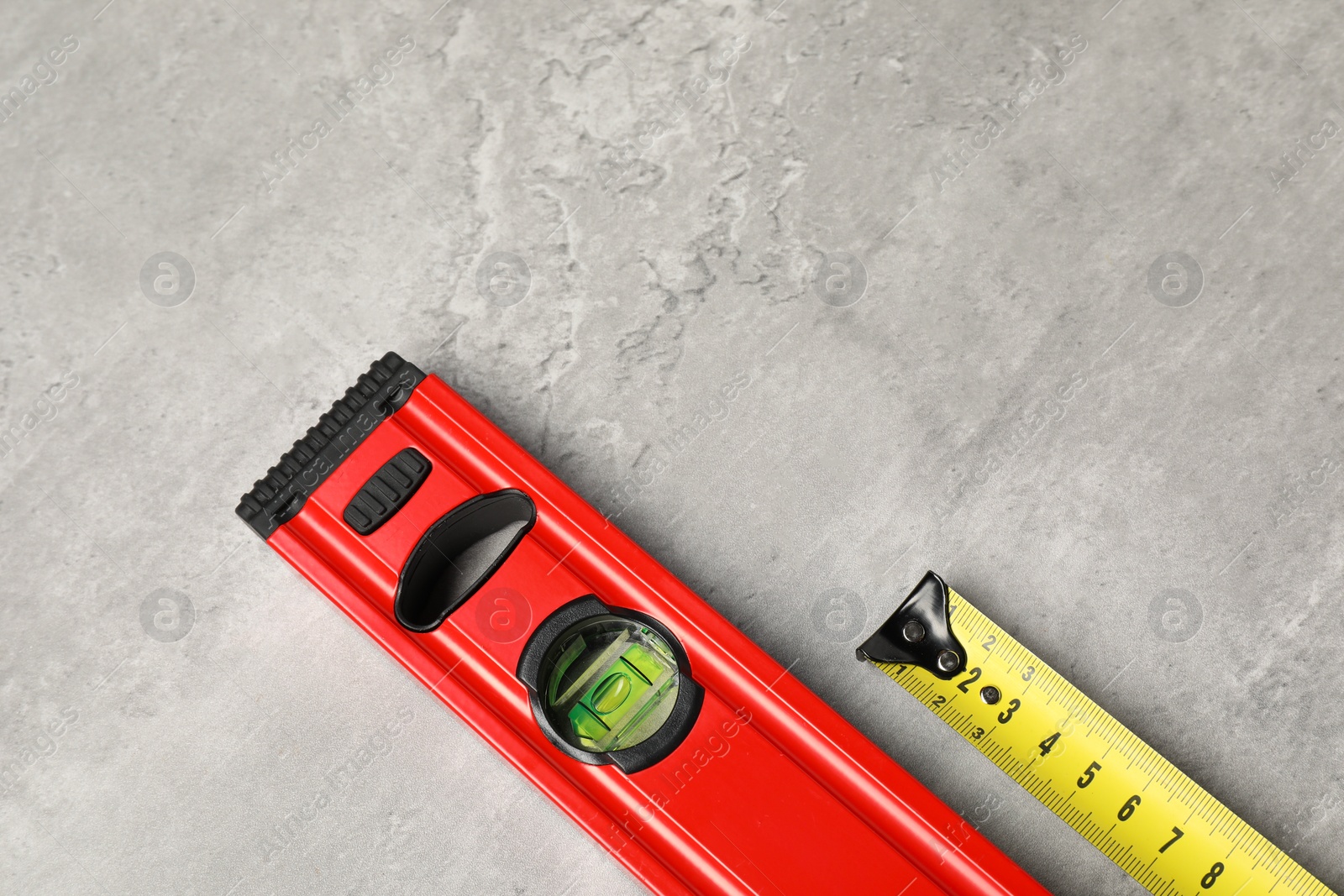 Photo of Building level and tape measure on grey table, top view. Space for text