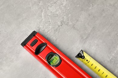 Building level and tape measure on grey table, top view. Space for text