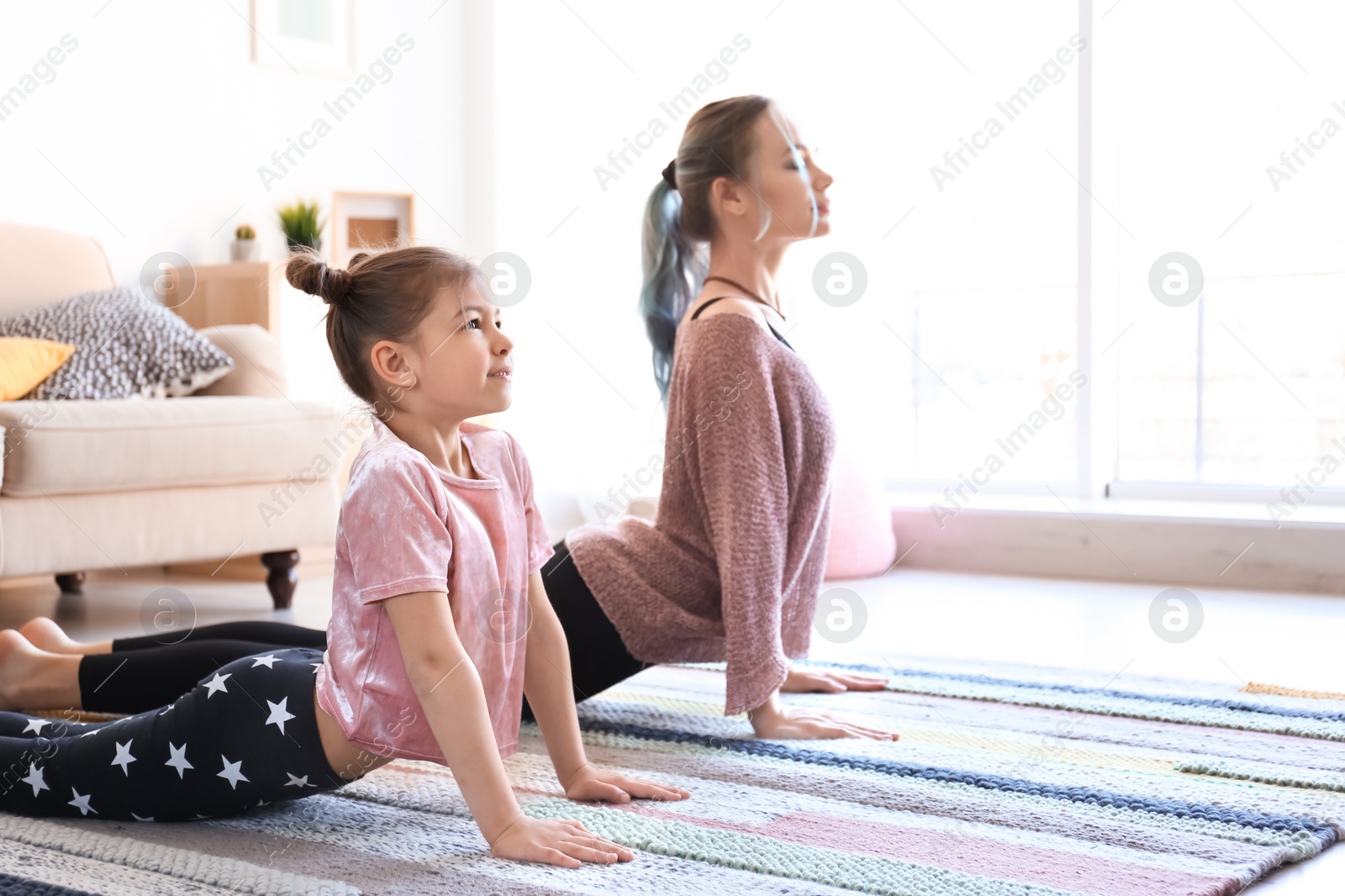 Photo of Young mother and her daughter practicing yoga at home