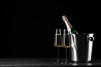 Photo of Glasses of champagne near bucket with bottle on black background, space for text