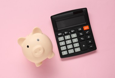 Calculator and piggy bank on pink background, top view