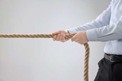 Photo of Dispute concept. Businessman pulling rope on light grey background, closeup