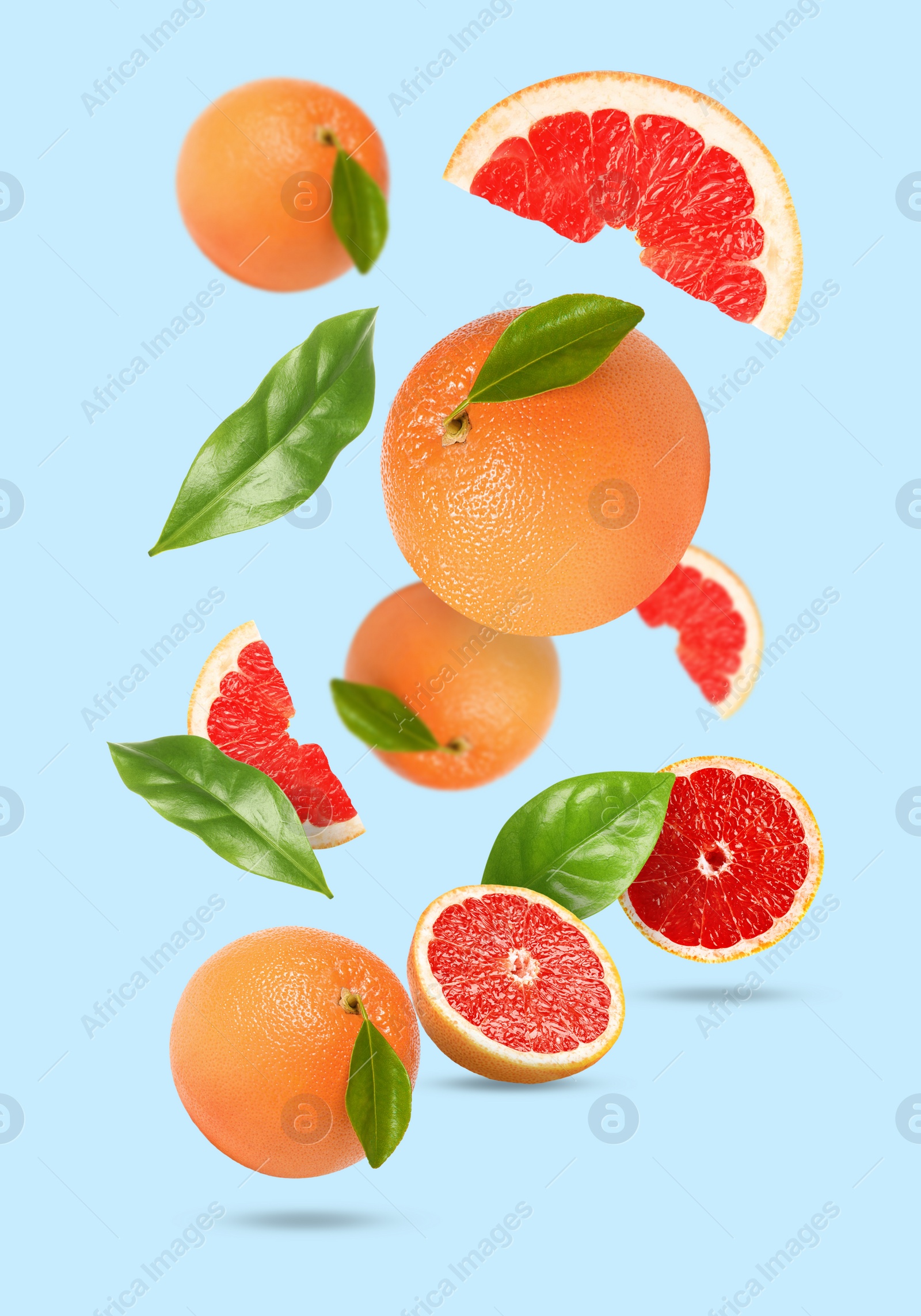 Image of Tasty ripe grapefruits and green leaves falling on light blue background