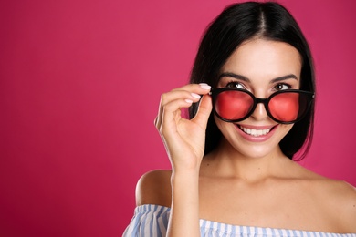 Beautiful woman wearing sunglasses on pink background, closeup. Space for text