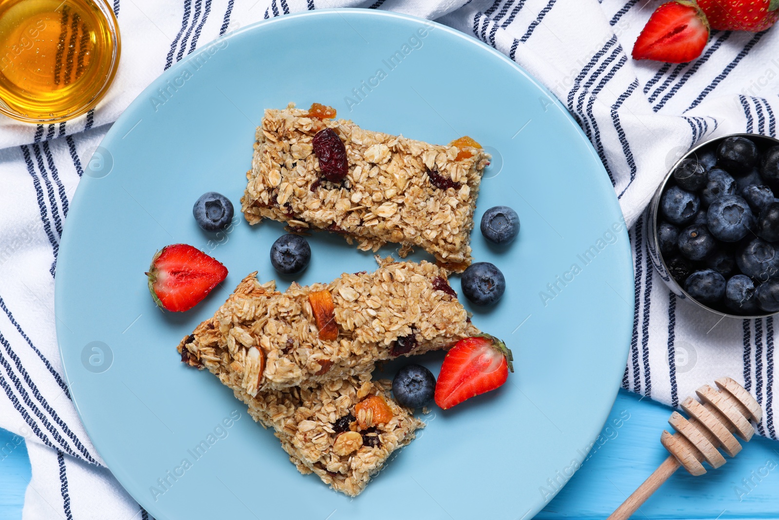 Photo of Tasty granola bars with berries and honey on light blue wooden table, flat lay