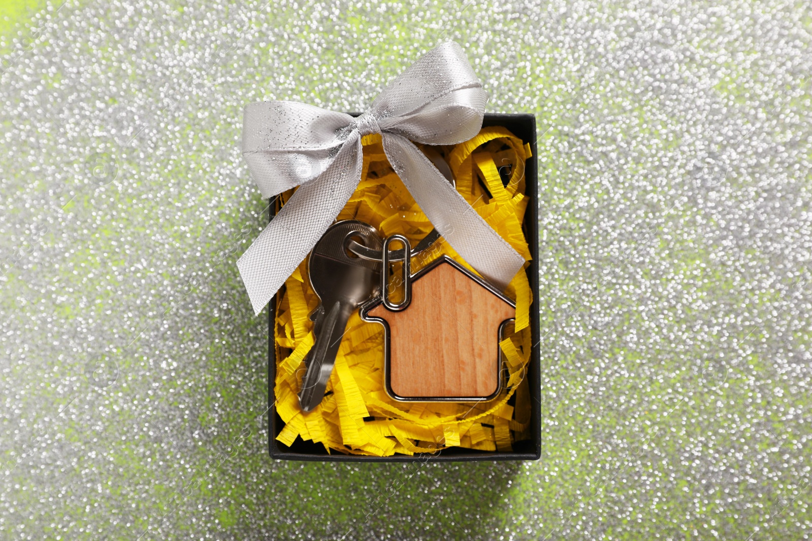 Photo of Key with trinket in shape of house, glitter and gift box on shiny surface, top view. Housewarming party