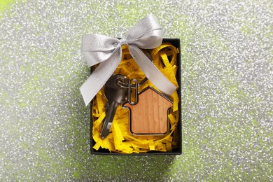 Key with trinket in shape of house, glitter and gift box on shiny surface, top view. Housewarming party