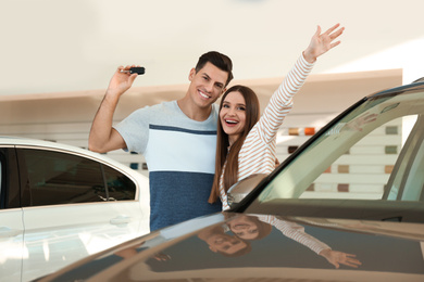 Happy couple with car key in modern auto dealership