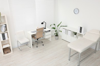 Photo of Modern medical office with doctor's workplace and examination table in clinic