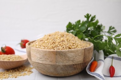 Photo of Raw bulgur in bowl, vegetables and parsley on table, closeup