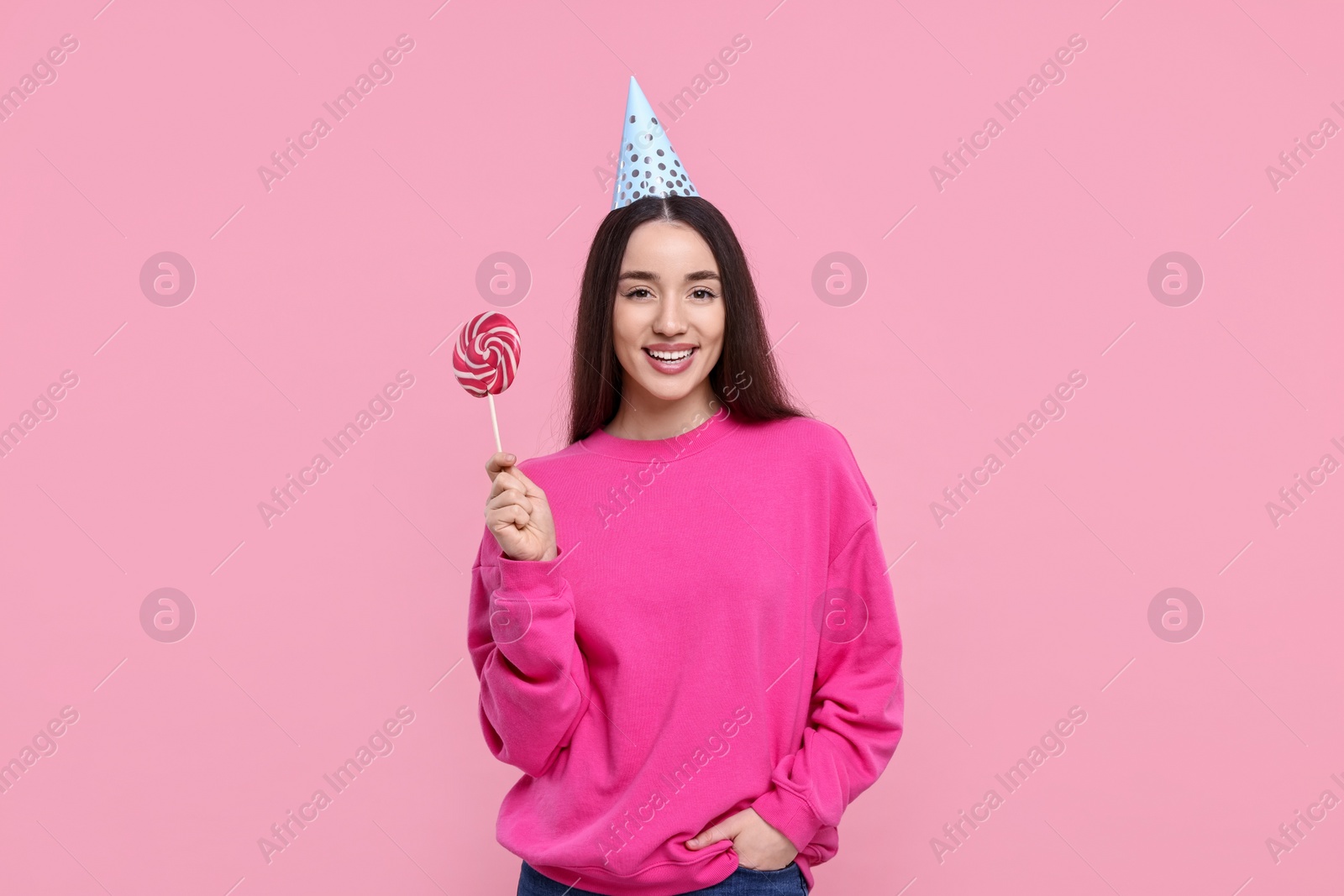 Photo of Woman in party hat holding lollipop on pink background