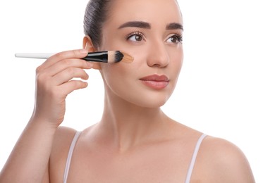 Woman applying foundation on face with brush against white background