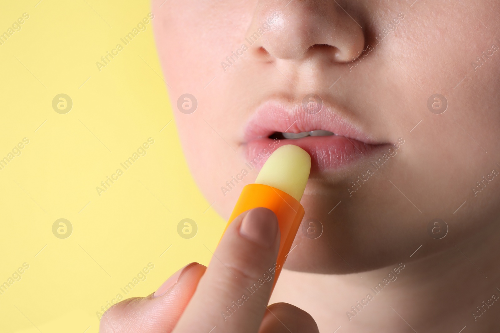 Photo of Woman applying hygienic lipstick on lips against yellow background, closeup