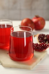 Photo of Tasty pomegranate juice in glasses and fresh fruits on white wooden table, closeup