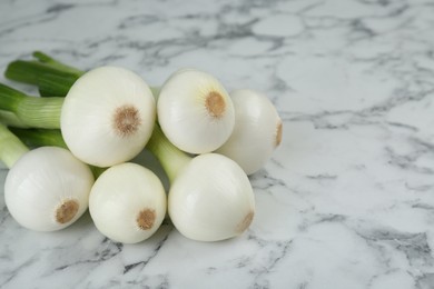 Photo of Whole green spring onions on white marble table, closeup. Space for text