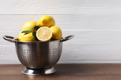 Fresh lemons and green leaves on wooden table. Space for text