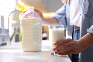 Young woman with gallon bottle of milk and glass at white countertop in kitchen, closeup