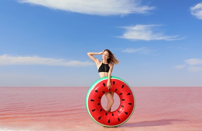 Beautiful woman with inflatable ring posing near pink lake on sunny day