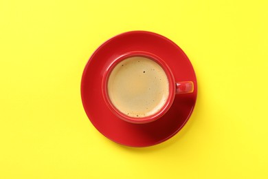 Tasty coffee in cup on yellow background, top view