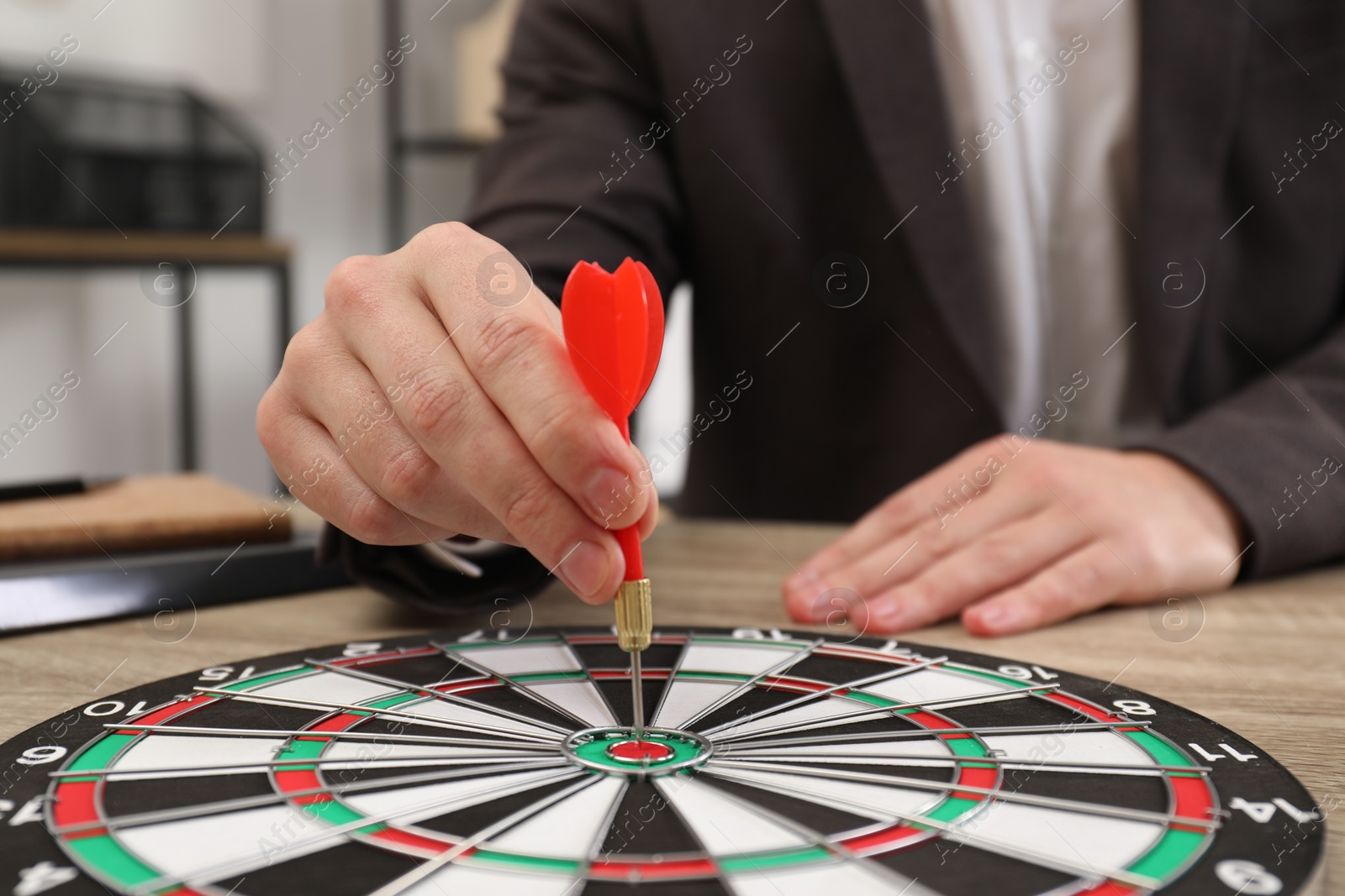 Photo of Business targeting concept. Man with dart aiming at dartboard at table indoors, closeup