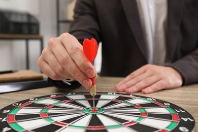 Business targeting concept. Man with dart aiming at dartboard at table indoors, closeup