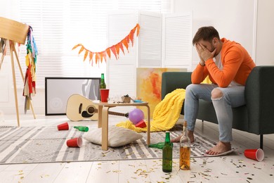 Tired drunk man on sofa in messy room after party