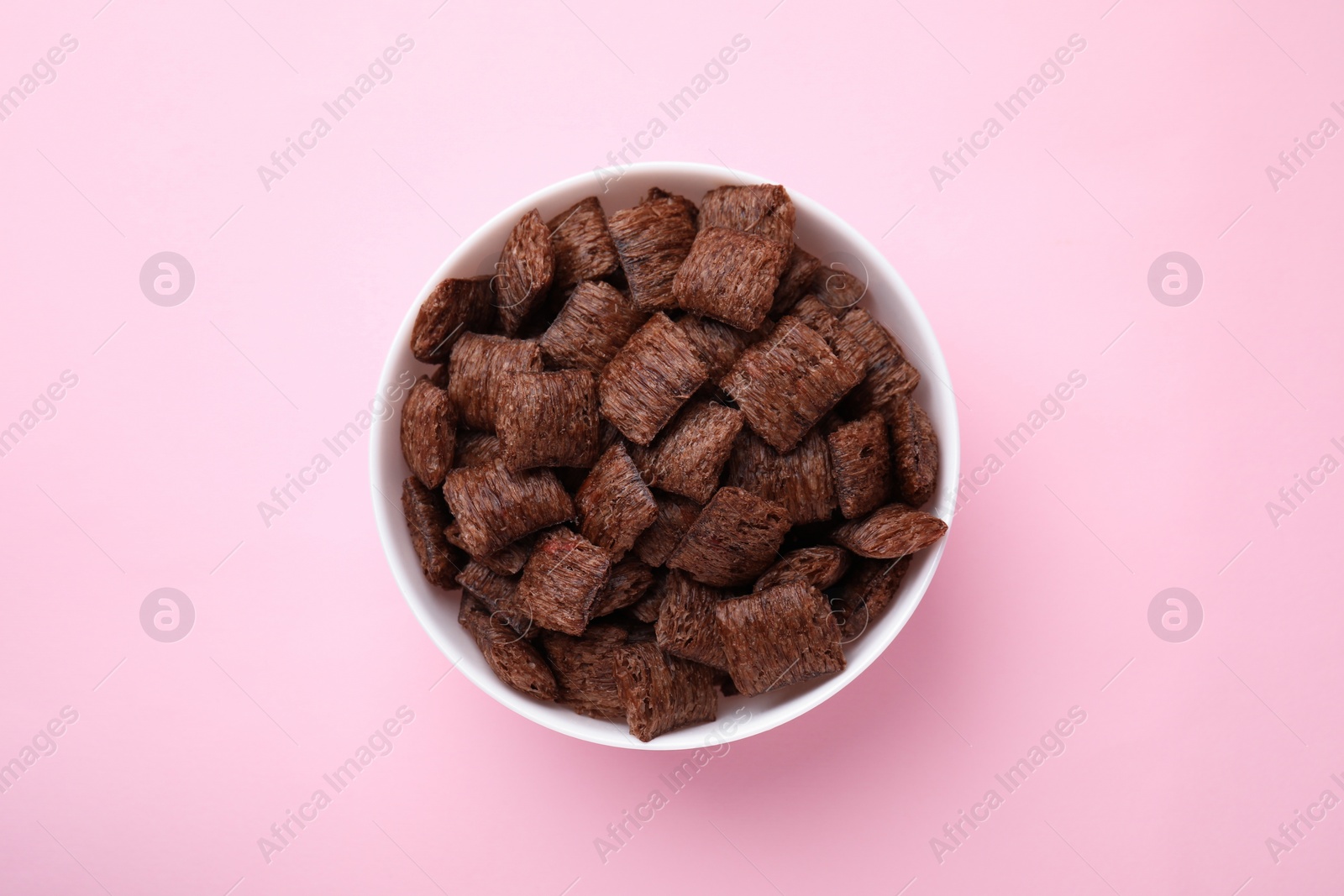 Photo of Chocolate cereal pads in bowl on pink table, top view