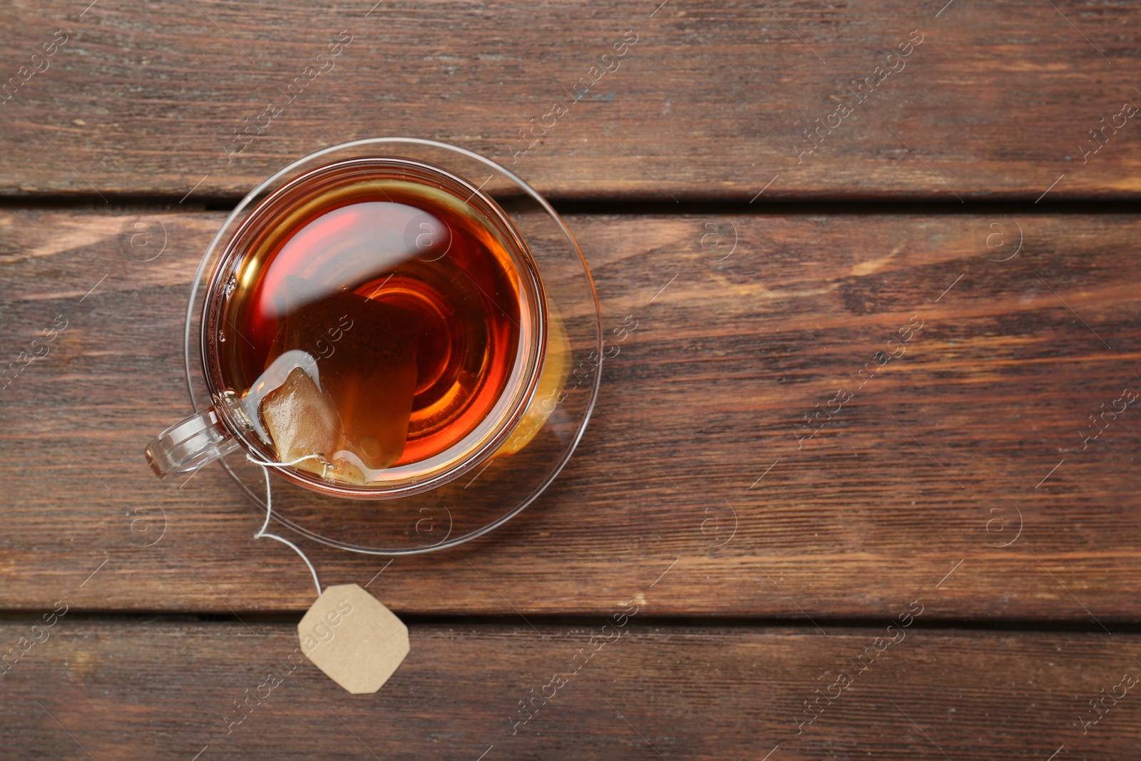 Photo of Brewing aromatic tea. Cup with teabag on wooden table, top view. Space for text