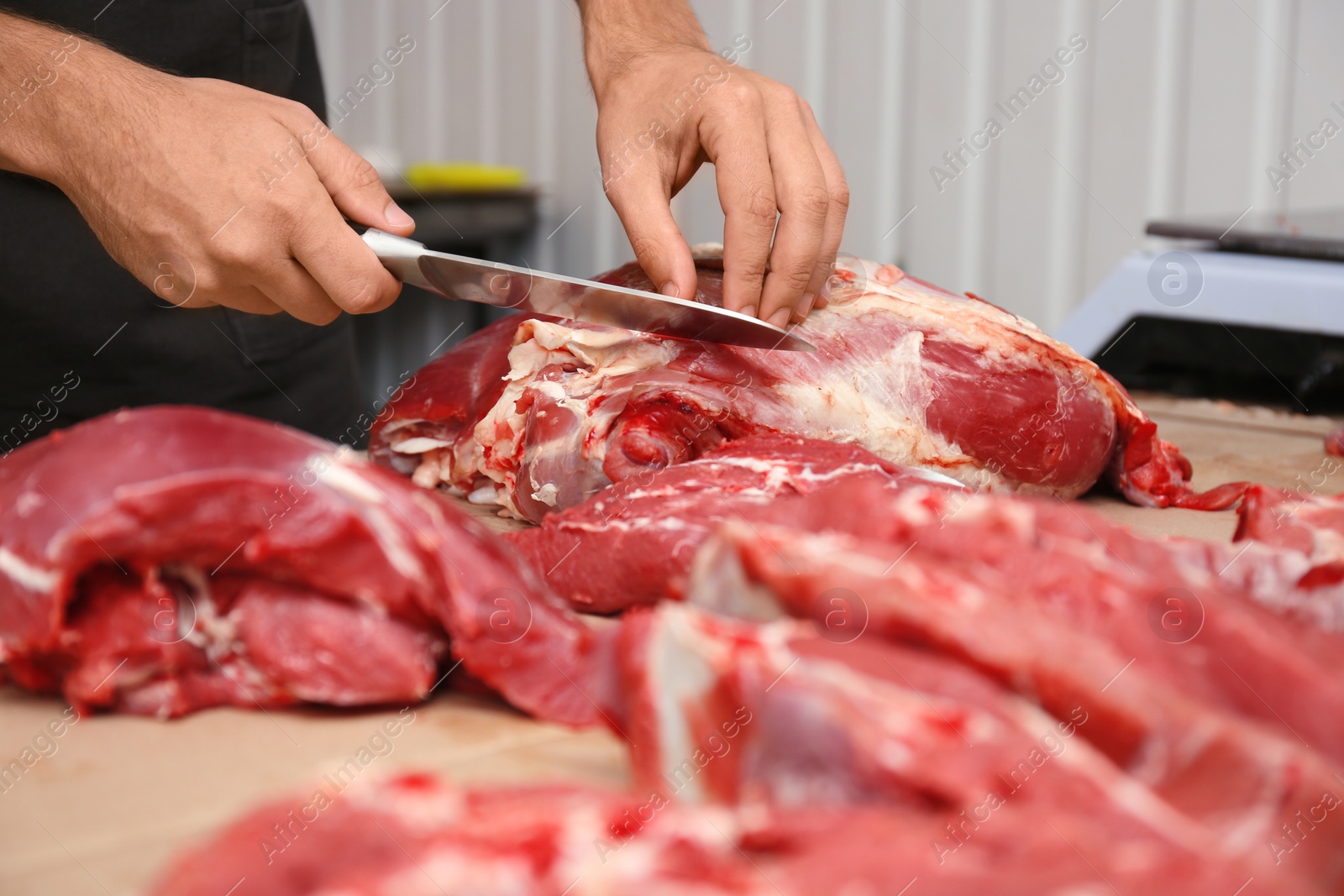 Photo of Butcher cutting fresh raw meat on counter in shop, closeup